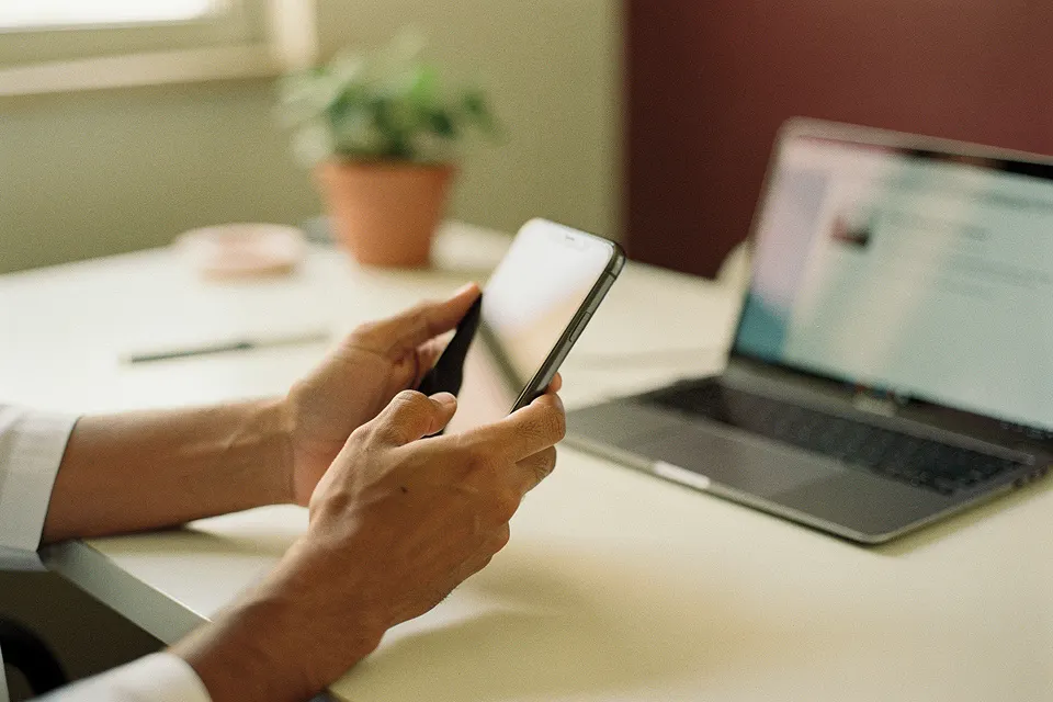 Profesional revisa la agenda del día en el celular, con la notebook abierta al lado