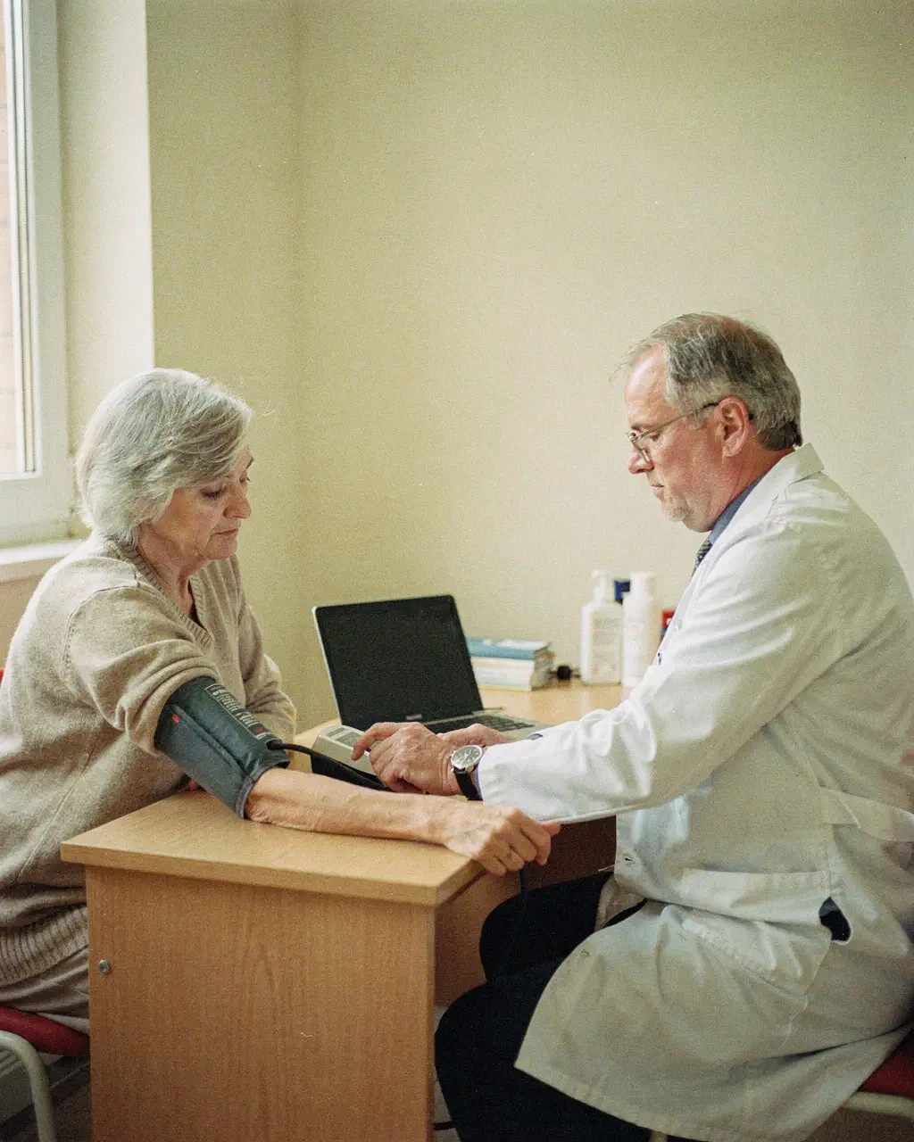 Médico clínico toma la presión a una paciente mayor sentada junto a su escritorio