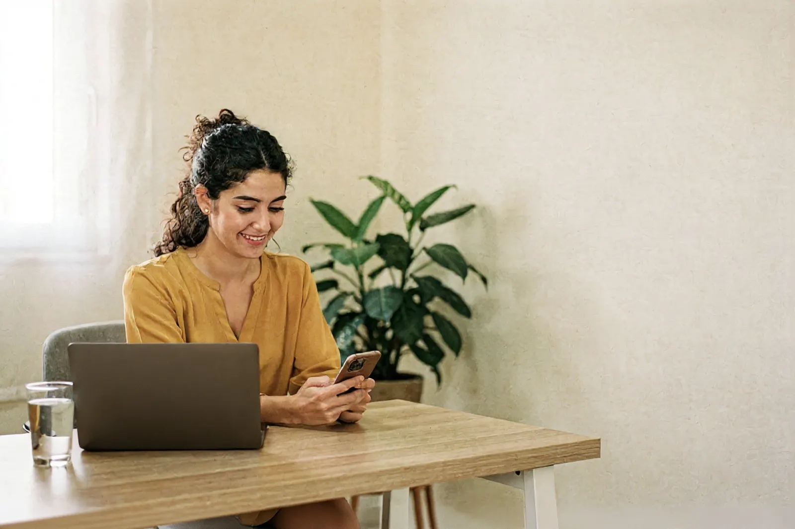 Profesional de la salud joven revisa el celular en su consultorio, con la notebook al lado